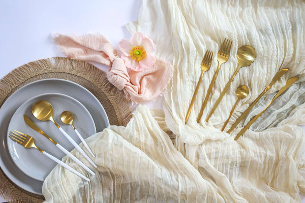 Flatlay of gold plated cutlery set on top of table runners