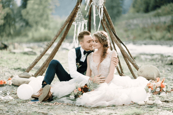 bride and groom on the ground in front of teepee wedding altar